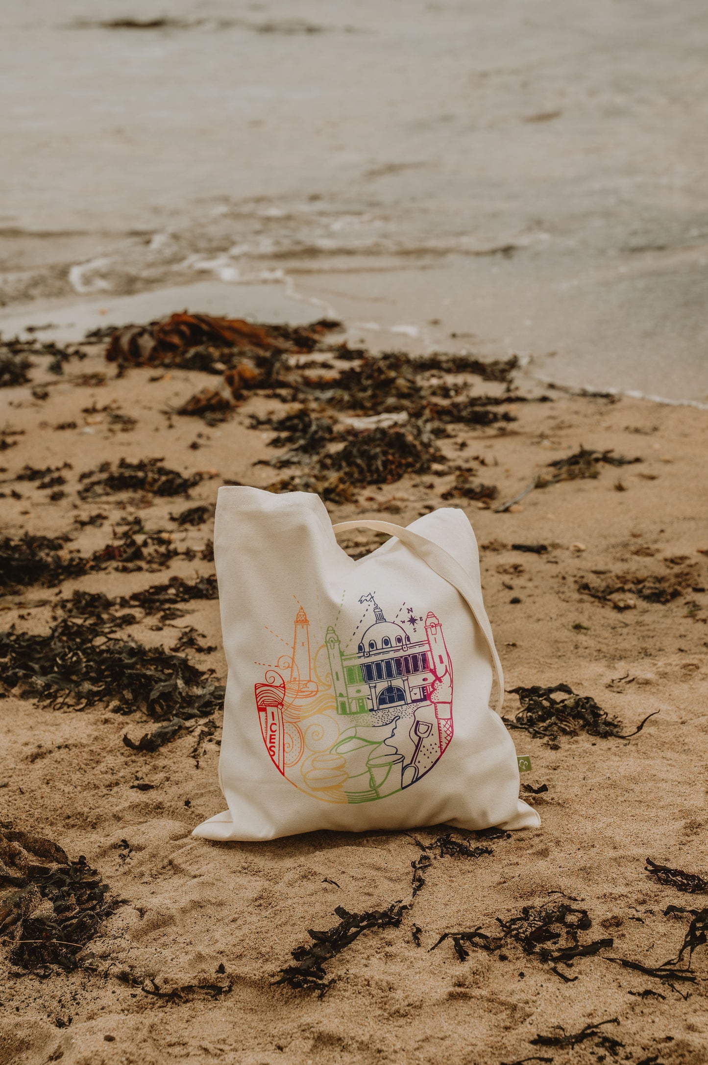 White tote bag with colorful design on a sandy beach