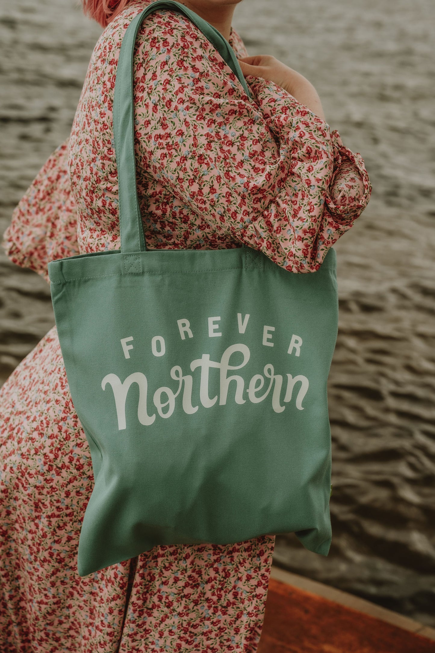 Person holding a green tote bag with 'Forever Northern' text by the North Sea