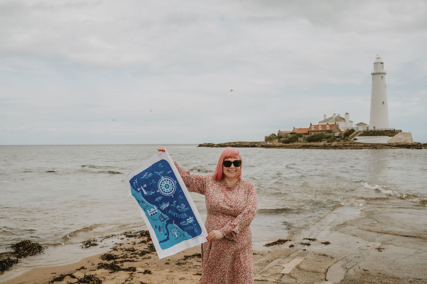 Person holding a blue and white tea towel by a lighthouse on a beach