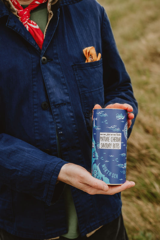 Person holding a blue canister with nature-themed design in a natural setting