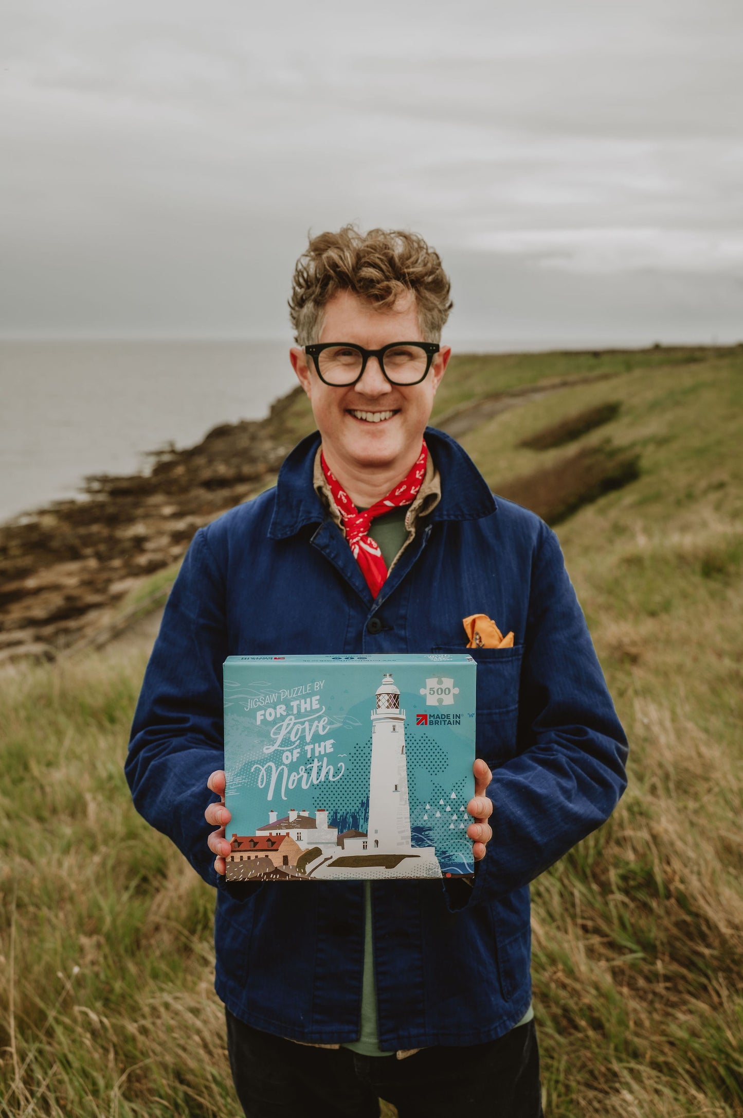 Person holding a jigsaw with a lighthouse illustration in a scenic outdoor setting