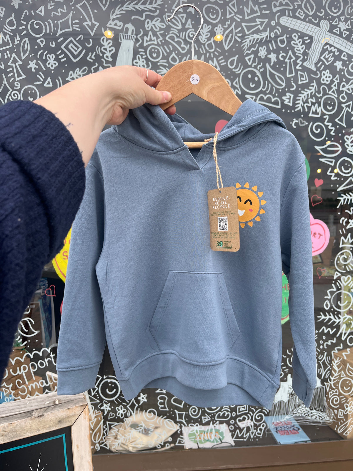 Blue sweatshirt held by a hand with a visible brand tag against a decorative background