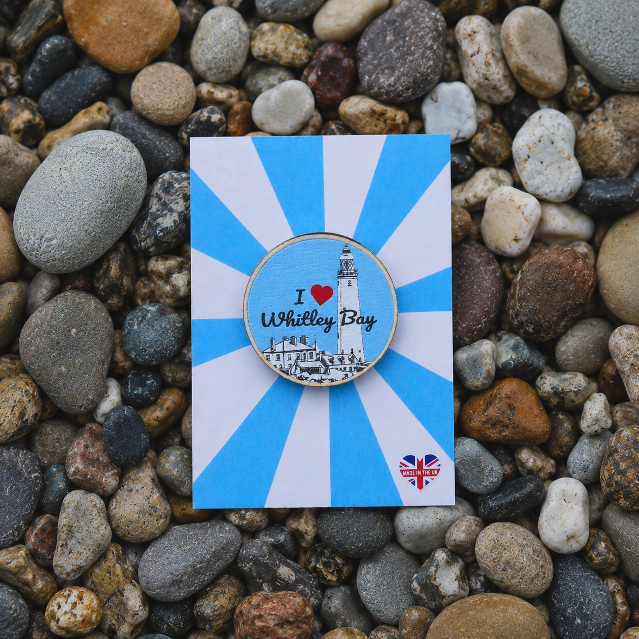 Badge with 'I ❤️ Whitley Bay' design on a blue and white striped card, placed on pebbles.
