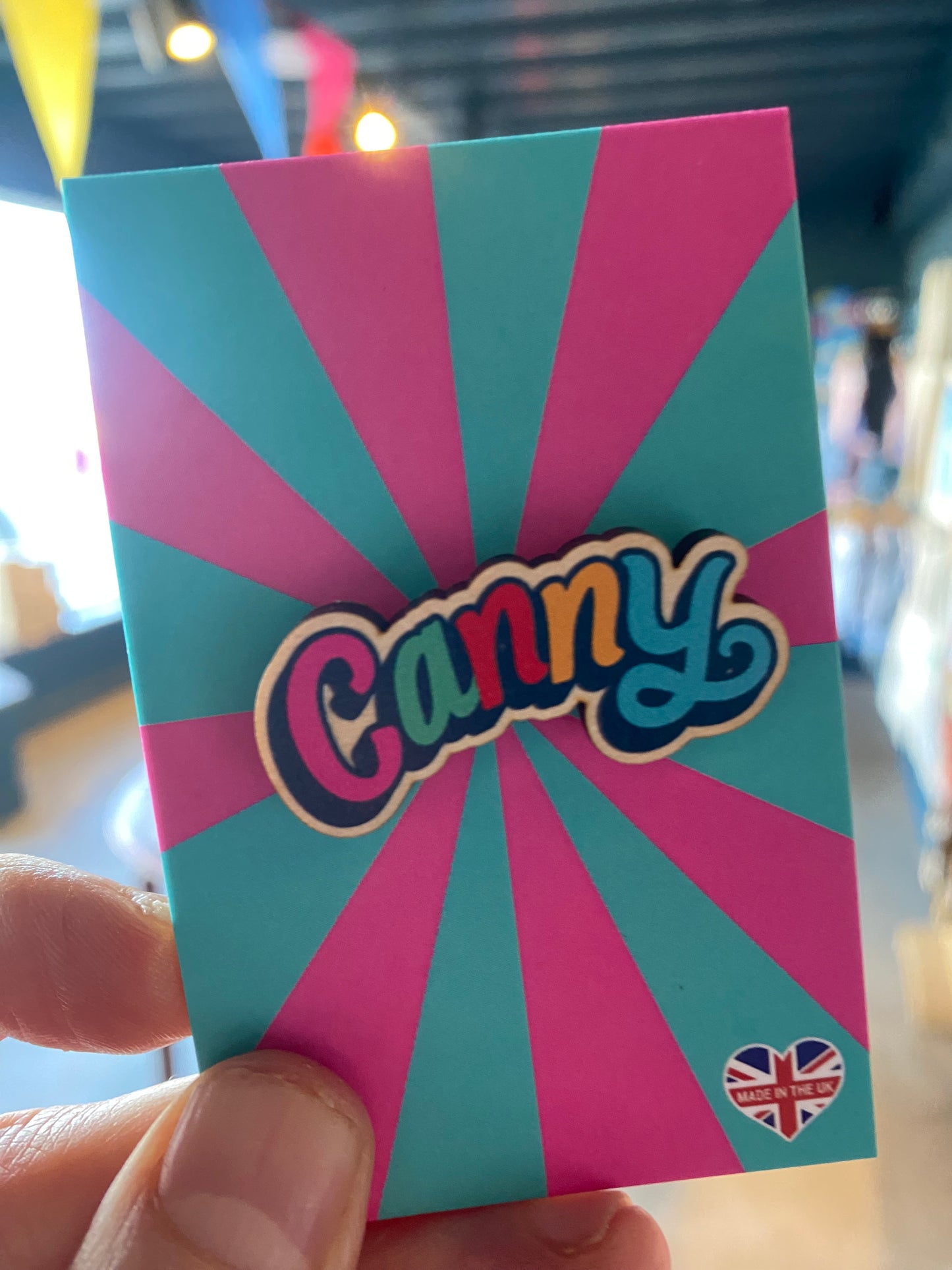 Colorful card with Canny wooden pin badge l held by a hand against a blurred background