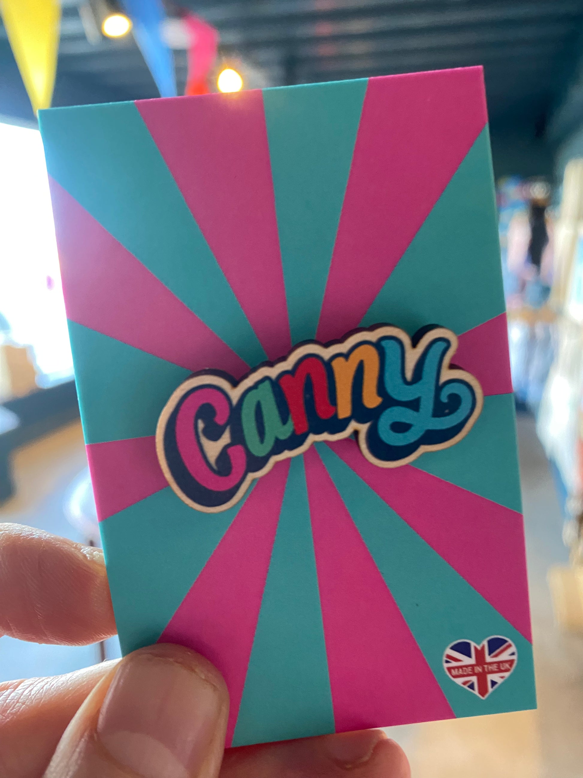 Colorful card with Canny wooden pin badge l held by a hand against a blurred background