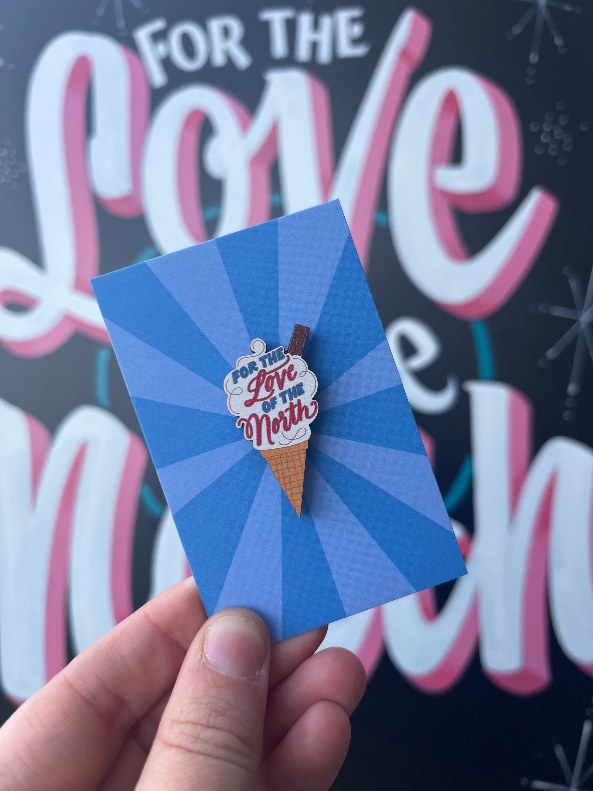 Hand holding a blue card with an ice cream cone-shaped pin badge.