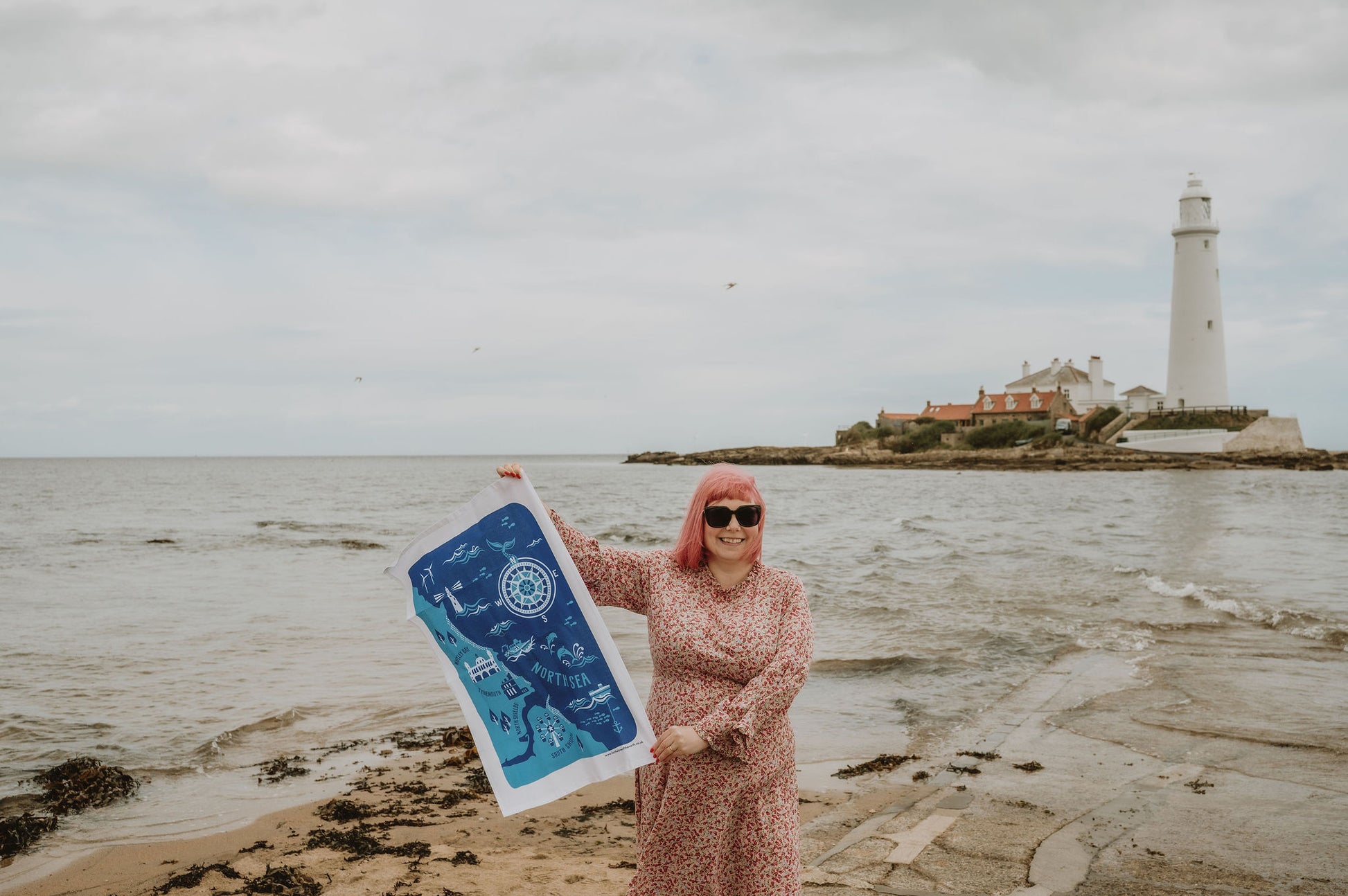 Person holding a blue and white tea towel by a lighthouse on a beach
