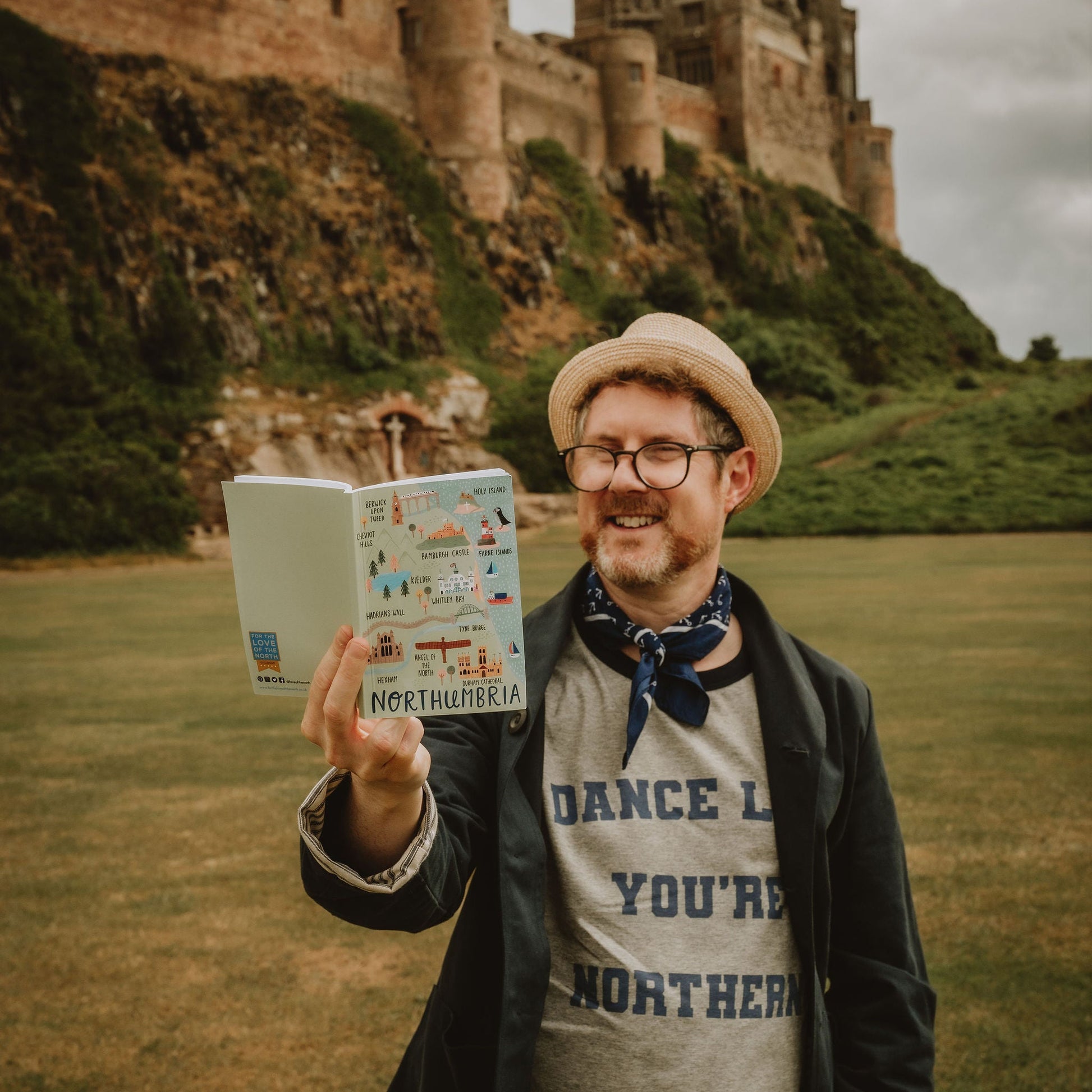 A person holding a Northumbria map A6 notebook with a castle in the background.