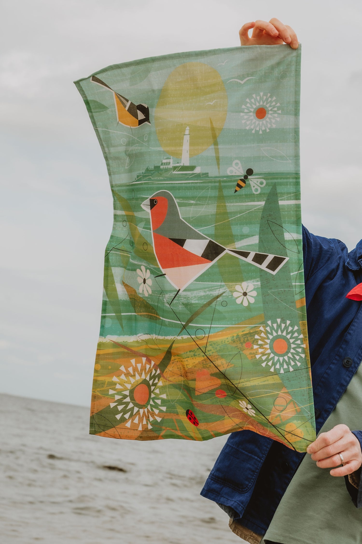 Person holding a colorful tea towel with a bird design against a neutral background