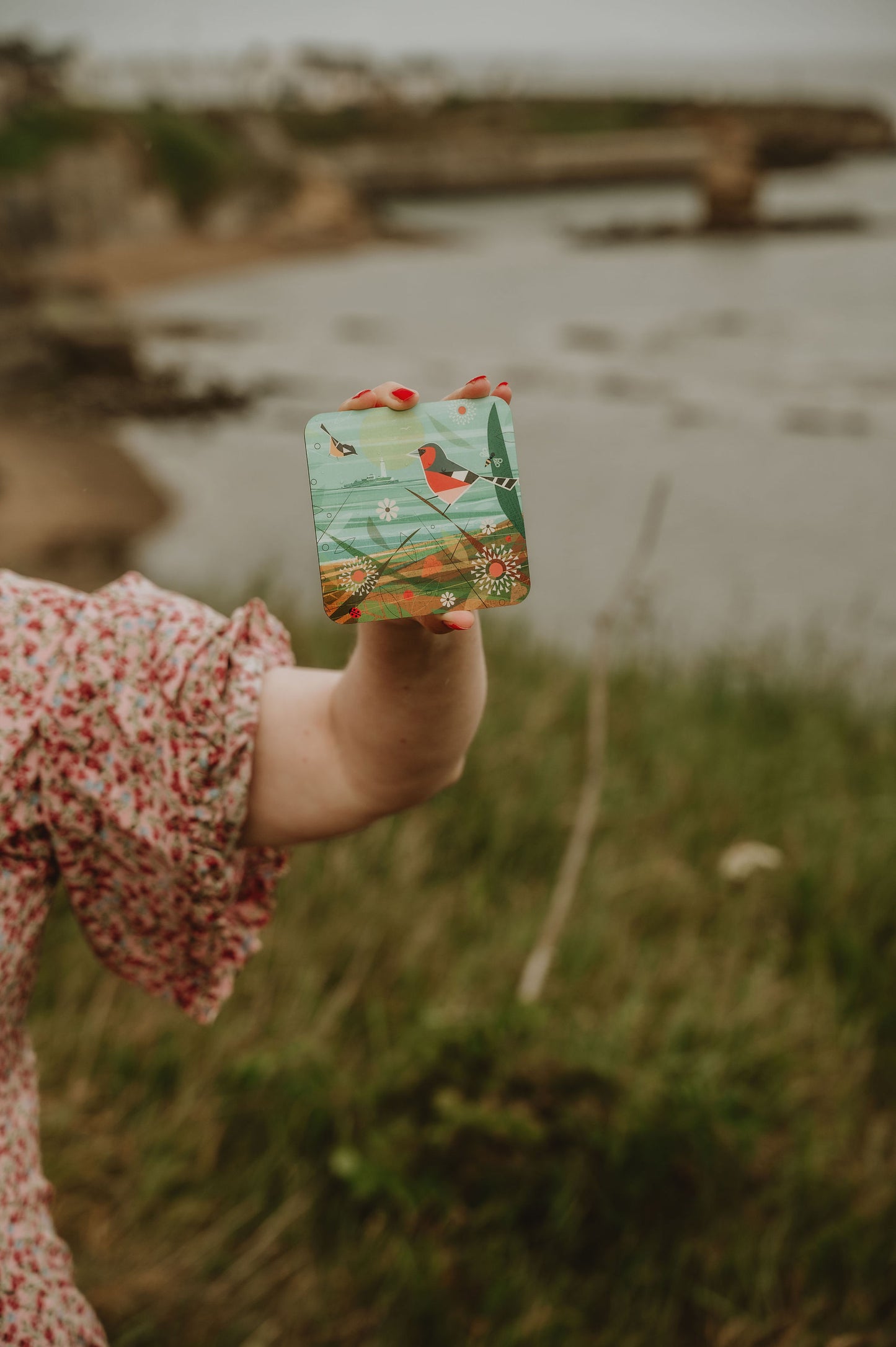 Person holding a colorful coaster with nature design outdoors by the North Sea.