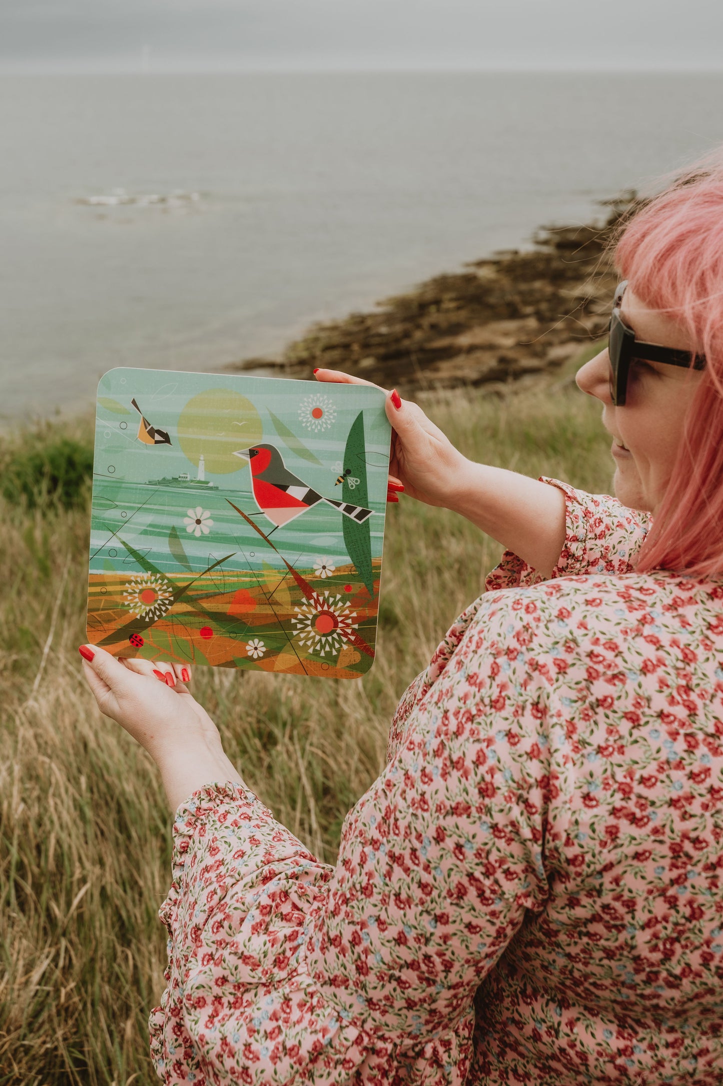 Person holding a placemat with a bird illustration outdoors by the North Sea