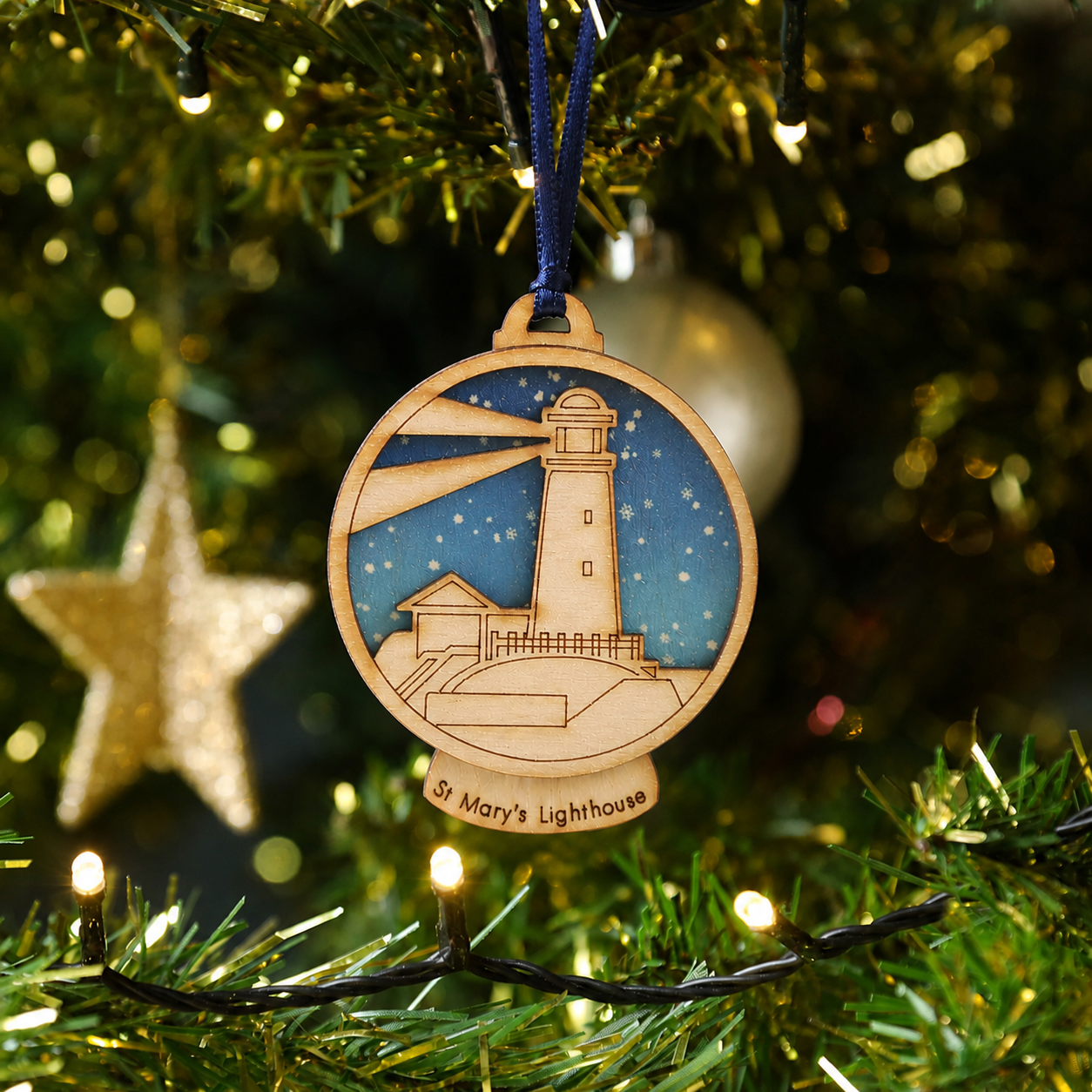 Wooden ornament of St. Mary's Lighthouse on a Christmas tree with lights and tinsel.