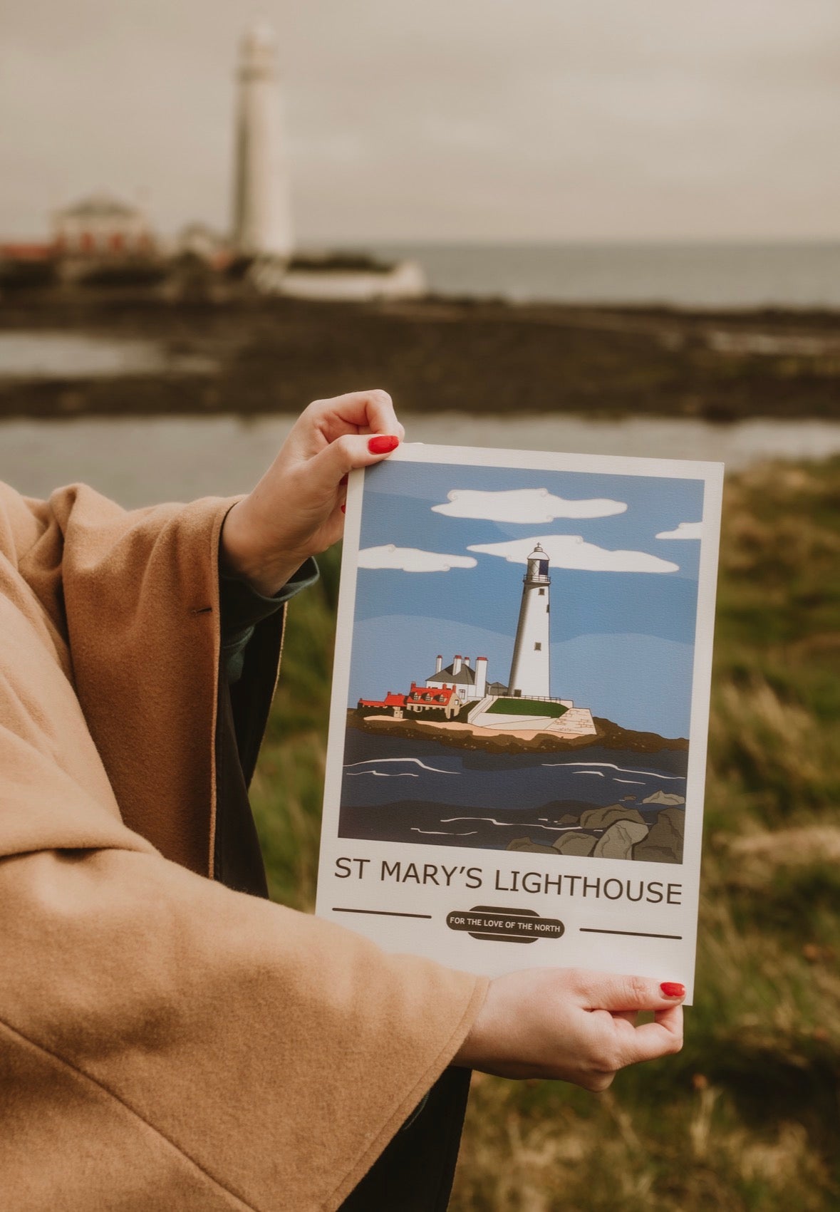 Person holding a poster of St Mary's Lighthouse with St Mary's Lighthouse, Whitely Bay in the background.