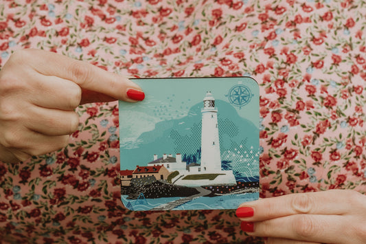 Hand holding a coaster with a lighthouse design against a floral background